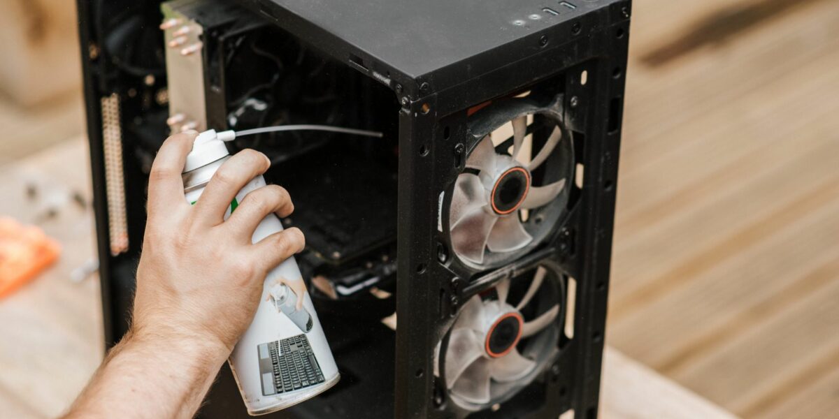 A user is cleaning the PC fans of their computer with a compressed air can.