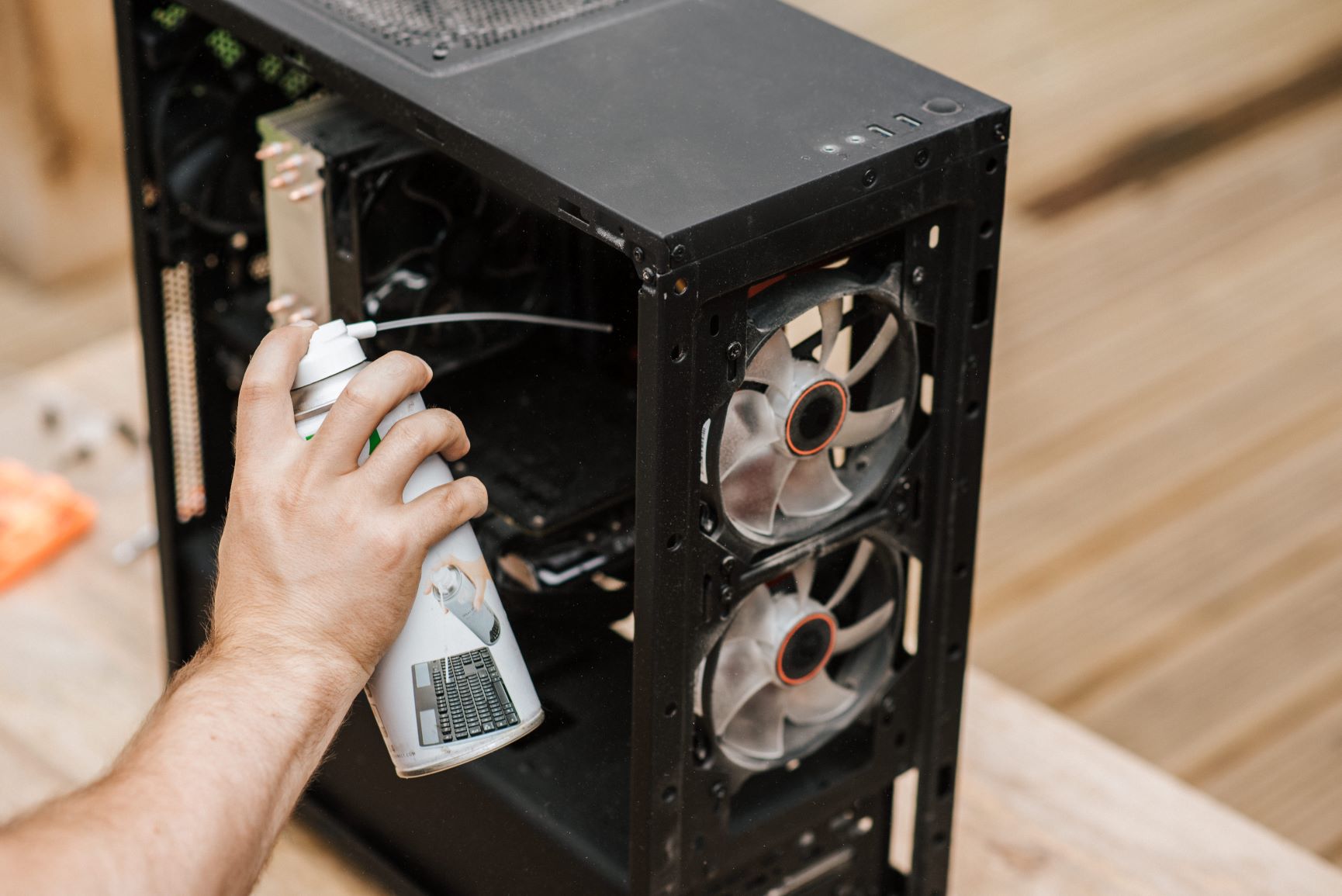 A user is cleaning the PC fans of their computer with a compressed air can.