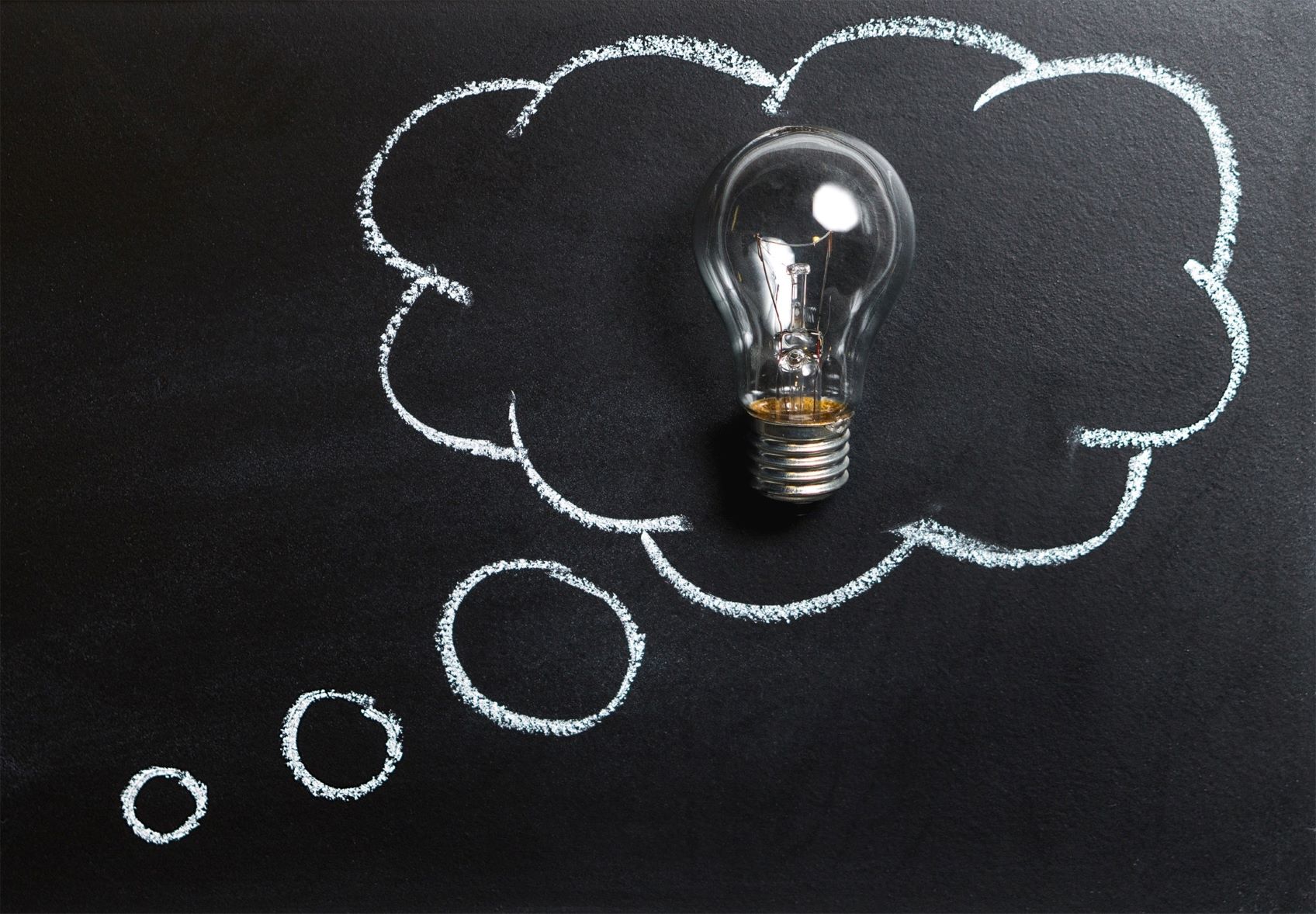 A chalk board with three white circles leading to a larger fluffy cloud with a lightbulb in the center to represent cloud services.