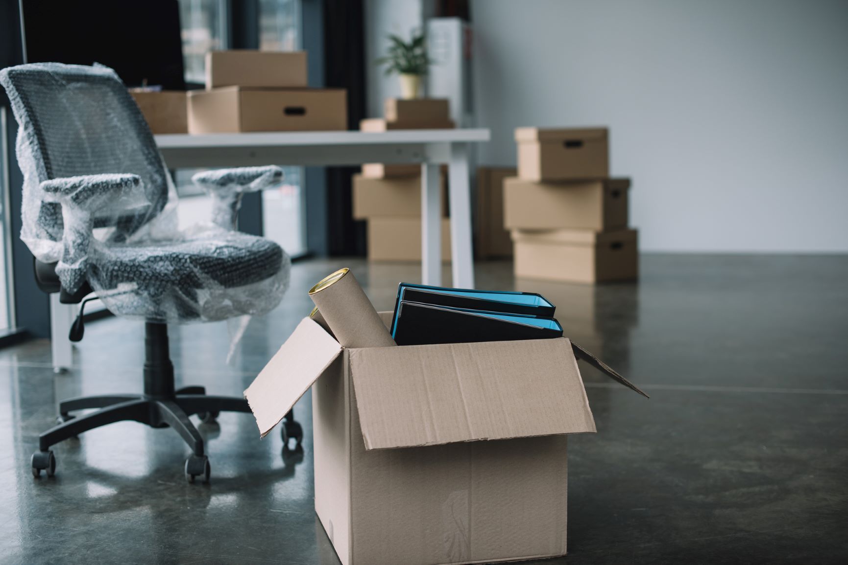 An office with IT resources such as computer hardware sit in a box on the floor by a desk computer.