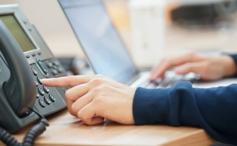 A worker at their desk uses their VoIP system, punching in numbers on their phone. Learn more about VoIP services