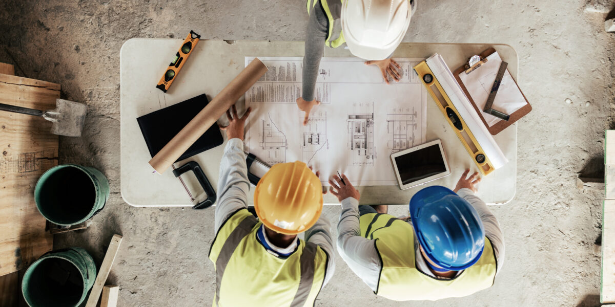 Three construction workers looking over plans on a table and on a tablet showing the importance of construction it services.