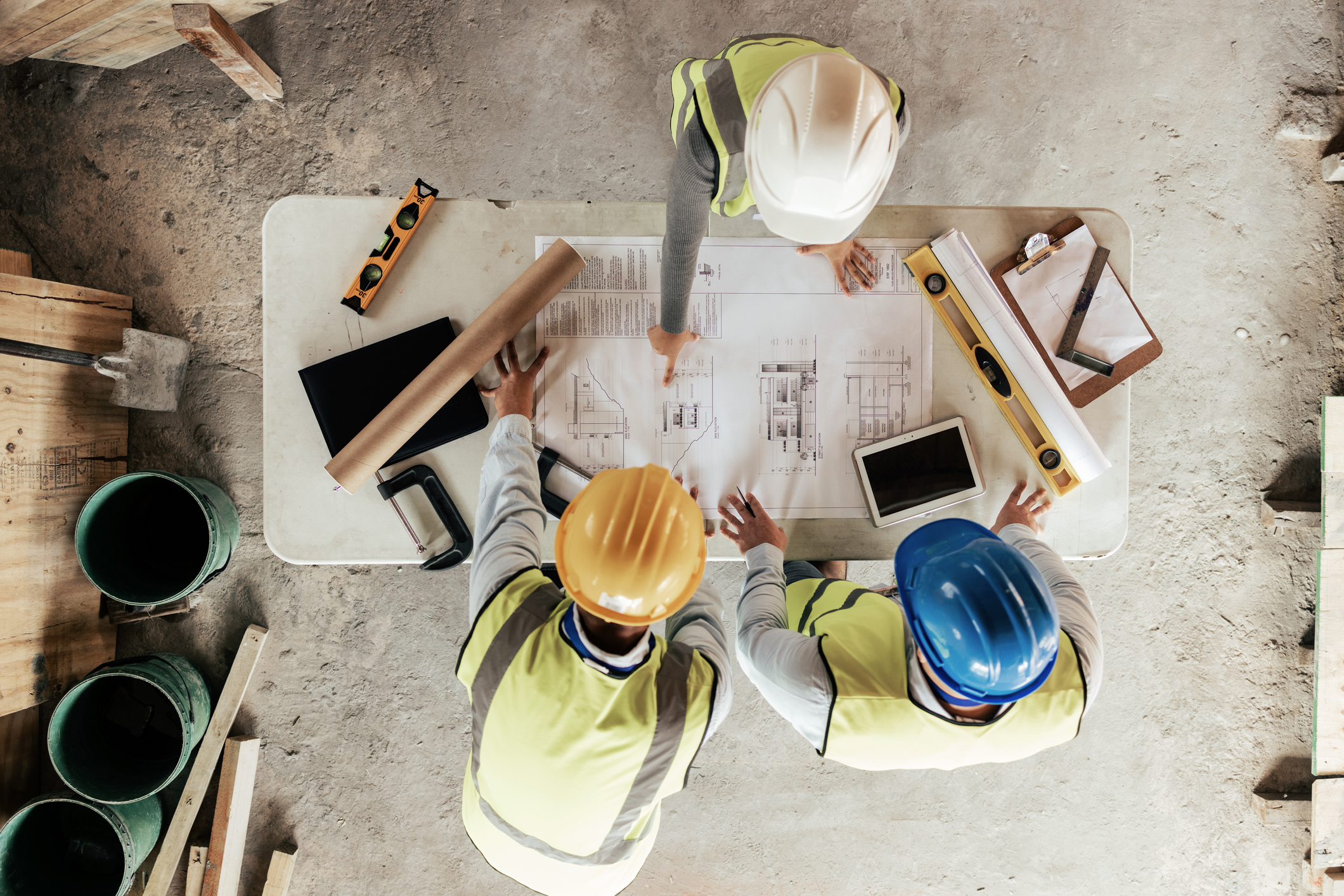 Three construction workers looking over plans on a table and on a tablet showing the importance of construction it services.