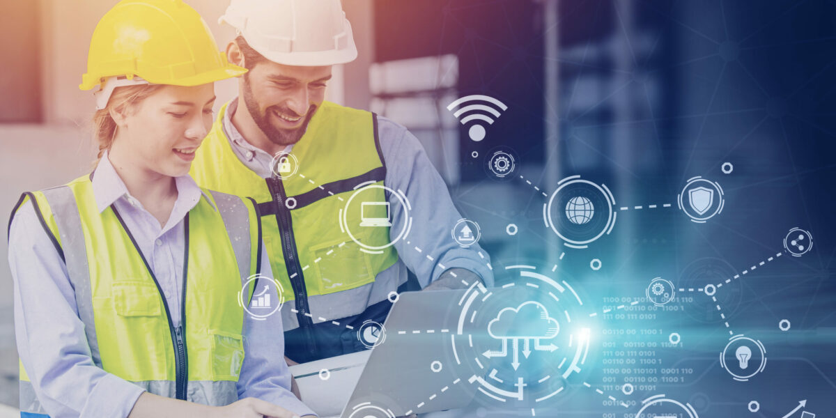 Two construction workers look at a computer with graphics of different business IT icons to represent construction technology.